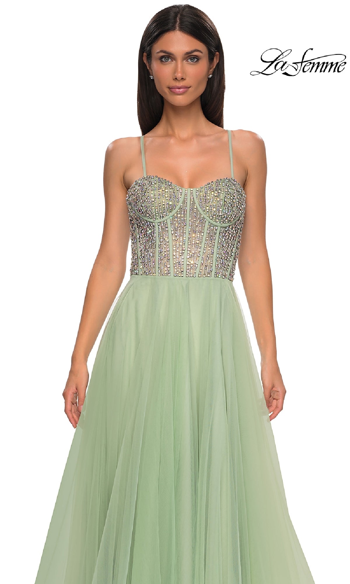 A woman models the La Femme 32703 Beaded-Corset Long Prom Dress—a light green evening gown with rhinestone beading, thin straps, and a flowing skirt—standing against a plain white background.